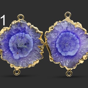 Puede incluir: Dos colgantes en forma de flor de cristal de amatista púrpura con detalles dorados y anillas de salto. Los colgantes miden aproximadamente 5 cm de diámetro.