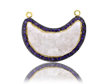 May include: A crescent moon shaped pendant with a white quartz center and a black and gold border. The border is set with small purple gemstones.