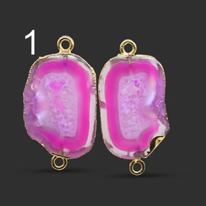 May include: Two pink agate gemstone pendants with gold-colored edges and loops. The pendants have a natural, irregular shape and a polished finish. The gemstones are a vibrant pink color with white and translucent areas.