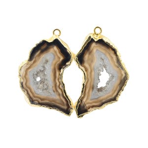 May include: Two agate gemstone pendants with gold-colored edges and a small loop at the top. The pendants have a natural, layered appearance with shades of brown, white, and black. The center of each pendant has a crystalline structure.