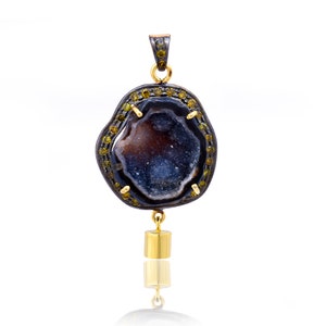 May include: A silver pendant with a black and blue agate geode, surrounded by a halo of yellow gemstones. The pendant hangs from a gold chain with a small gold bead at the bottom.