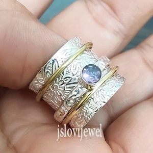May include: A silver and gold spinning ring with a purple gemstone. The ring is decorated with a floral pattern.