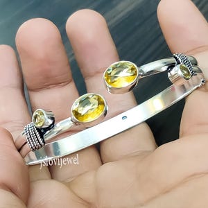 Op de afbeelding: Zilveren armband met drie gele edelstenen. De armband is open en heeft een getextureerd ontwerp.