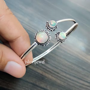 Peut inclure: Bracelet en argent avec trois pierres d'opale serties dans des montures en argent ornées. Le bracelet est ouvert et réglable.