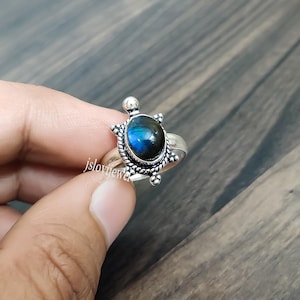 May include: A sterling silver ring featuring a turtle-shaped setting with a central oval labradorite gemstone displaying blue iridescence. The metalwork includes beaded and twisted wire details around the stone. The text jslovijewel is visible.