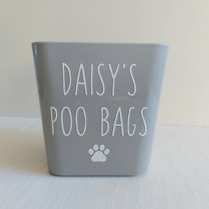 May include: A grey plastic container with the text "Daisy's Poo Bags" and a white paw print.