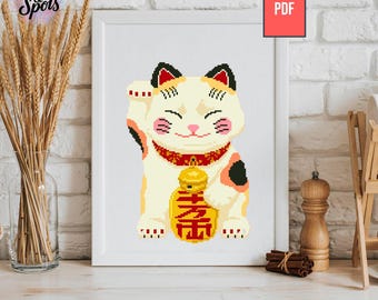 May include: A framed cross-stitch of a Maneki-neko, or lucky cat, with a raised paw. The cat is cream-colored with black and orange accents, a red collar, and a gold coin. The image is displayed on a white surface.