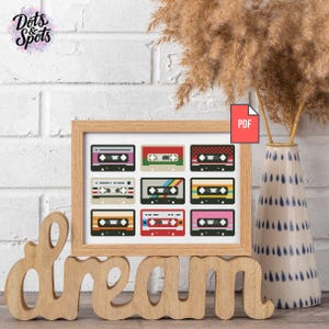 Könnte beinhalten: Ein gerahmter Druck mit neun pixeligen Kassettenband-Designs in verschiedenen Farben. Der Rahmen ist hellbraun, und das Wort "dream" steht in Holzbuchstaben vor dem Rahmen. Im Hintergrund eine Vase mit getrockneten Pflanzen.