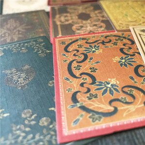 May include: A set of decorative paper cards with a vintage book cover design. The cards feature a variety of patterns and colors, including red, orange, brown, and black. The cards are perfect for scrapbooking, card making, or other craft projects.