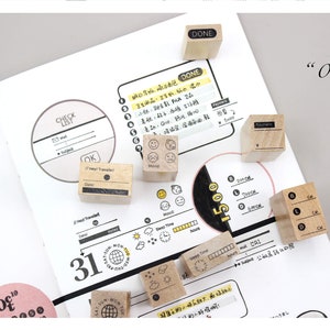 Puede incluir: Sellos de madera con iconos y texto, incluyendo "DONE", "Payment" e indicadores de estado de &aacute;nimo, sobre una p&aacute;gina de planificador. La p&aacute;gina presenta una lista de verificaci&oacute;n, elementos de calendario y otros elementos de planificaci&oacute;n.
