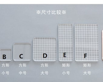 Puede incluir: Comparación de seis láminas de sellos de acrílico transparente en diferentes tamaños y formas. Las láminas están etiquetadas con las letras A a F y tienen líneas de cuadrícula. El texto "※尺寸比较※" está escrito en negro en la parte superior de la imagen. Se muestra un iPhone 7 para comparar el tamaño.
