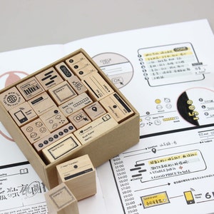 Puede incluir: Un conjunto de sellos de madera con varios iconos y texto, incluyendo "Lectura" y "Hecho", dispuestos en una caja de cart&oacute;n. Los sellos se utilizan en una p&aacute;gina de cuaderno con notas e ilustraciones manuscritas.