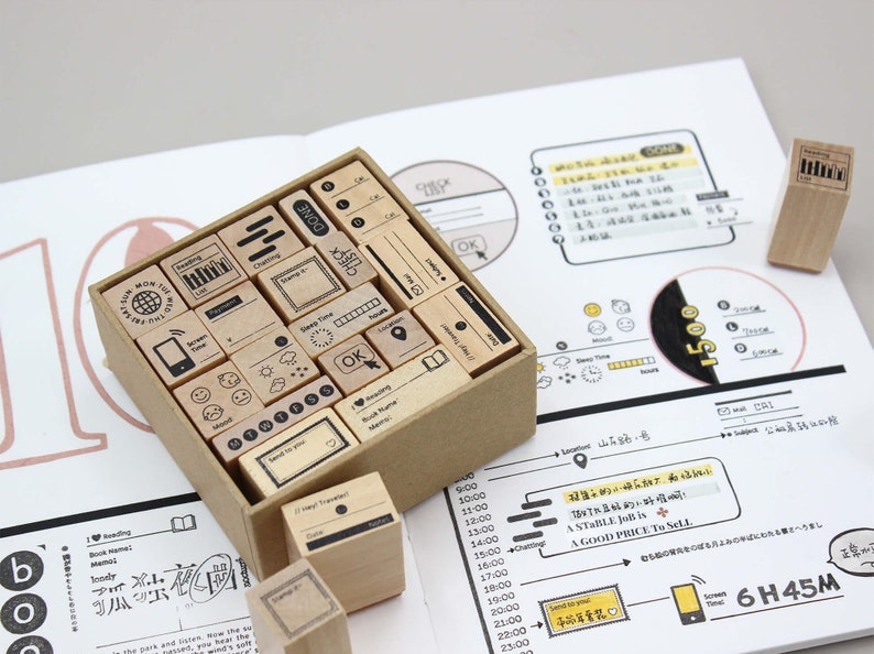 Puede incluir: Un conjunto de sellos de madera con varios iconos y texto, incluyendo "Lectura" y "Hecho", dispuestos en una caja de cart&oacute;n. Los sellos se utilizan en una p&aacute;gina de cuaderno con notas e ilustraciones manuscritas.