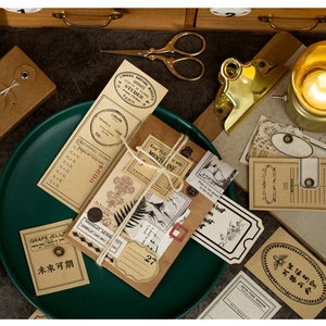 Może przedstawiać: Zestaw vintage'owych naklejek i etykiet papierowych z r&oacute;żnymi wzorami i tekstami, w tym "Worm Syrup", "GRAPE JELLY", "STUDER PARIS", "Keep True with Mentline" i "未来可期". Naklejki są ułożone na zielonym talerzu i brązowej powierzchni.