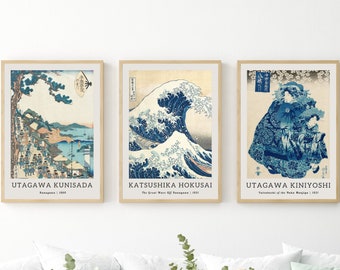 May include: Three framed prints of Japanese woodblock prints. The left print is a landscape scene with a mountain, a river, and a village. The middle print is a famous wave print with a large wave crashing over a boat. The right print is a scene of a mountain with a waterfall. The prints are all in blue and white tones.