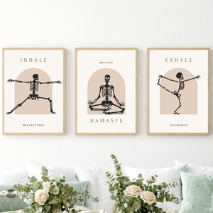 Puede incluir: Tres impresiones enmarcadas con esqueletos negros en diferentes posturas de yoga. Las impresiones tienen un fondo melocotón con forma de arco. El texto en las impresiones dice "INHALE", "BALANCE NAMASTE" y "EXHALE".