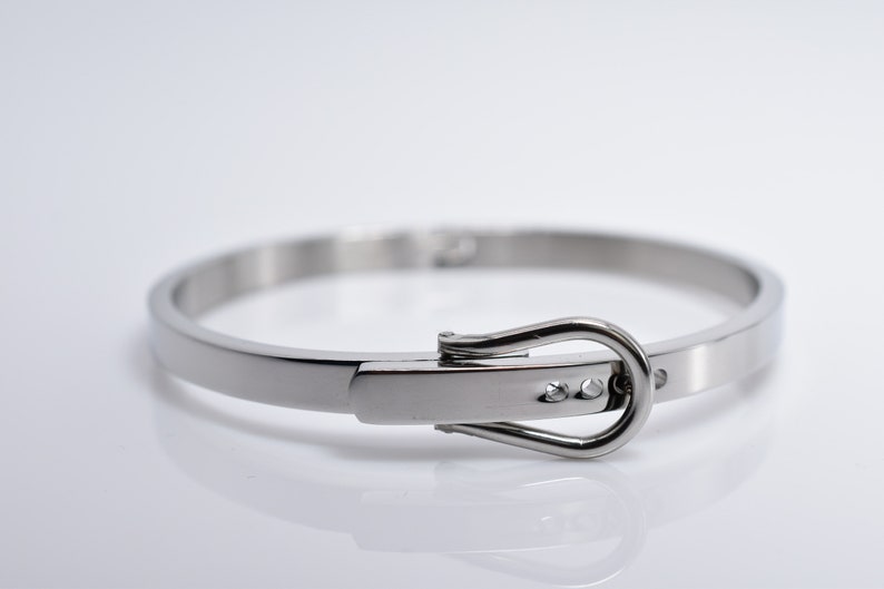 Op de afbeelding: Een zilveren armband met een gespsluiting. De gesp heeft drie kleine, heldere stenen.