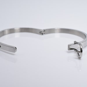 Op de afbeelding: Een zilveren armband met een scharniergesp en een rij kleine zwarte steentjes.
