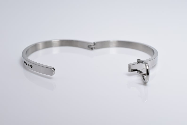 Op de afbeelding: Een zilveren armband met een scharniergesp en een rij kleine zwarte steentjes.