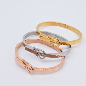 Op de afbeelding: Drie gouden, zilveren en ros&eacute;gouden armbandjes met een gespsluiting. De armbandjes zijn op elkaar gestapeld.