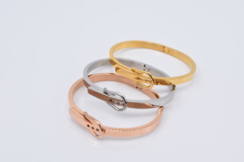 Op de afbeelding: Drie gouden, zilveren en ros&eacute;gouden armbandjes met een gespsluiting. De armbandjes zijn op elkaar gestapeld.