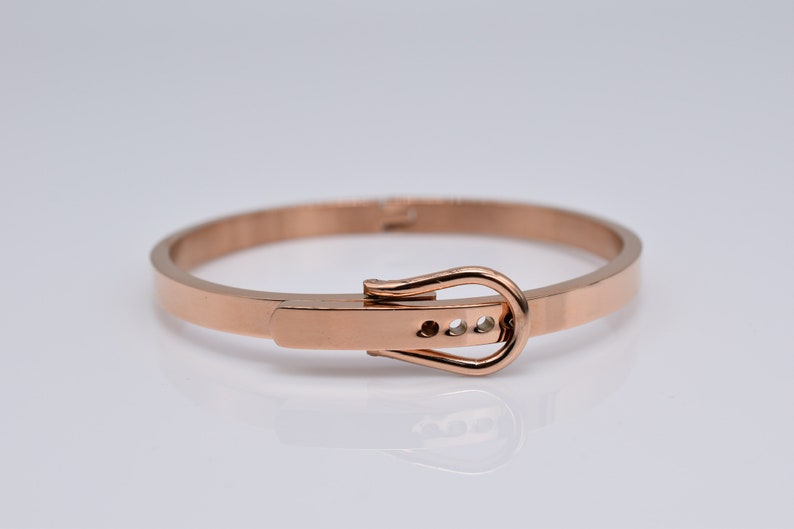 Op de afbeelding: Een armband van ros&eacute;goudkleurig metaal met een gespsluiting. De gesp heeft een kleine rij heldere stenen.