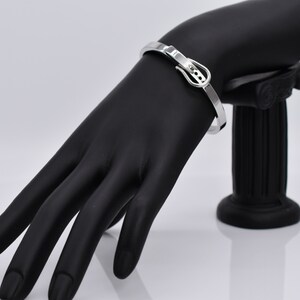 Op de afbeelding: Zilveren armband met een gespsluiting. De armband is op een zwarte mannequinhand.