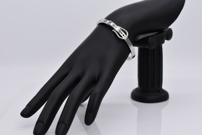 Op de afbeelding: Zilveren armband met een gespsluiting. De armband is op een zwarte mannequinhand.