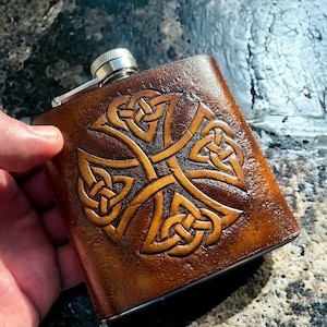 May include: A brown leather hip flask with a Celtic knot design embossed in gold. The flask has a silver cap and is a great gift for any whisky lover.