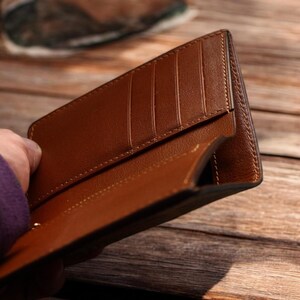 May include: Open brown leather wallet with multiple card slots. The wallet is held open, revealing the interior and the card slots. The leather appears to be smooth and well-crafted, with a warm, natural color.