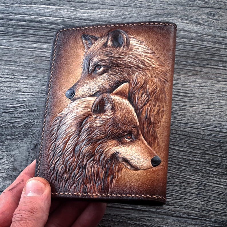 May include: A brown leather wallet with a tooled design of two wolves. The wolves are facing the same direction, with one wolf's head resting on the other wolf's shoulder.