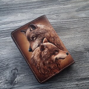 May include: A brown leather notebook cover with a tooled design of two wolves. The wolves are facing each other, with one wolf's head turned slightly to the side. The cover has a stitched edge.