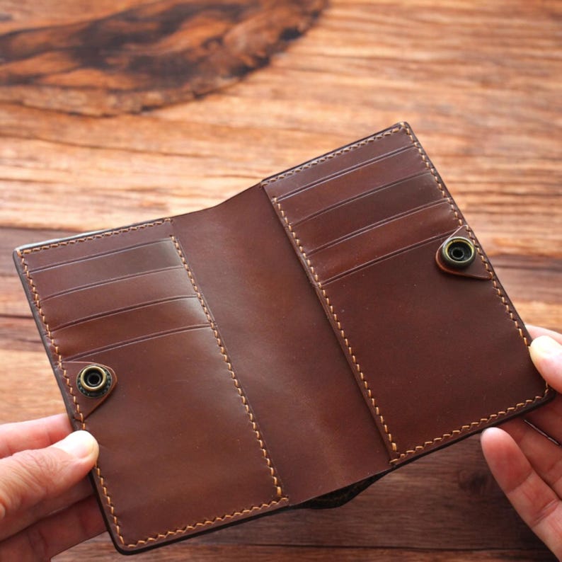 May include: Open brown leather wallet with multiple card slots and snap closures. The wallet is made of smooth, high-quality leather and features detailed stitching. The interior is a lighter shade of brown than the exterior.