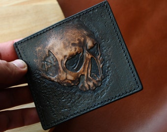 May include: A black leather wallet with a tooled skull design. The skull is embossed in a copper color.