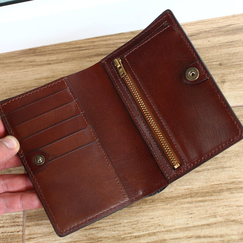 May include: A brown leather wallet with a zippered pocket and multiple card slots. The wallet is open and the interior is visible.