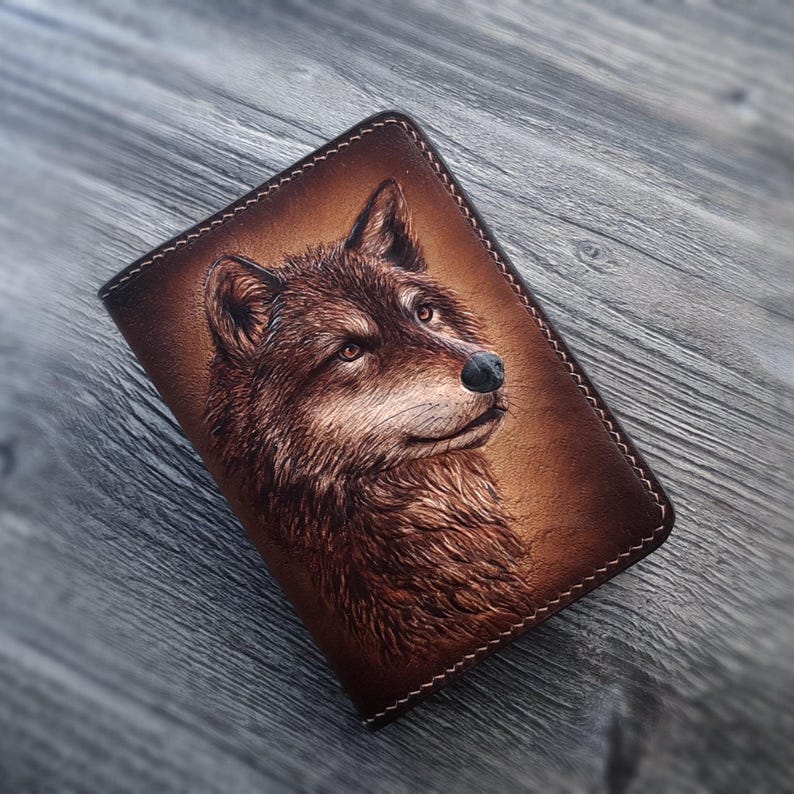 May include: A brown leather notebook cover with a detailed embossed image of a wolf's head. The wolf's fur is depicted in shades of brown and the eyes are a light brown color.