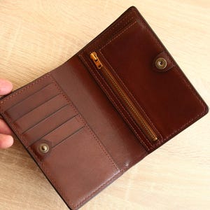 May include: A brown leather wallet with a zippered pocket and multiple card slots. The wallet is open and the interior is visible.