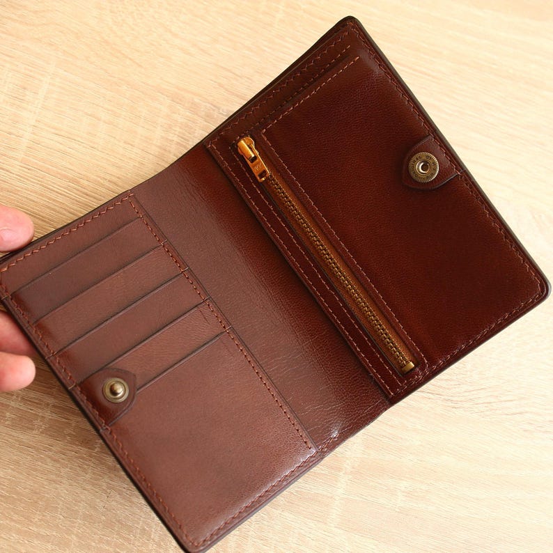 May include: A brown leather wallet with a zippered pocket and multiple card slots. The wallet is open and the interior is visible.