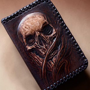May include: A rectangular dark brown leather wallet featuring a detailed embossed skull design on the front surface. The edges of the wallet are finished with a decorative braided leather lacing pattern that secures the perimeter of the item.