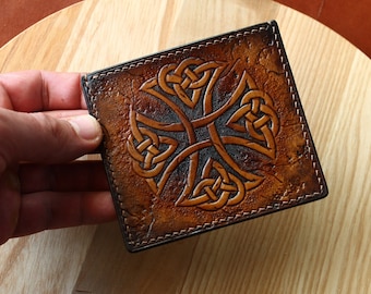 May include: A brown leather wallet with a Celtic knot design embossed on the front. The wallet has a stitched edge.