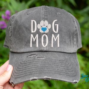 Pode incluir: Um bon&eacute; de beisebol cinza desbotado com o texto "Dog Mom" bordado em branco com uma pegada de pata e um cora&ccedil;&atilde;o azul no centro.