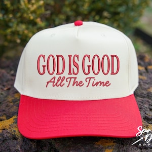 K&ouml;nnte beinhalten: Eine cremefarbene Baseballkappe mit einem leuchtend roten Schirm und einem roten Knopf an der Oberseite. Auf der Vorderseite befindet sich der gestickte rote Schriftzug "GOD IS GOOD" in serifenbetonter Schrift, gefolgt von "All The Time" in Schreibschrift.