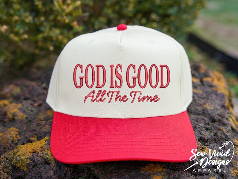 K&ouml;nnte beinhalten: Eine cremefarbene Baseballkappe mit einem leuchtend roten Schirm und einem roten Knopf an der Oberseite. Auf der Vorderseite befindet sich der gestickte rote Schriftzug "GOD IS GOOD" in serifenbetonter Schrift, gefolgt von "All The Time" in Schreibschrift.