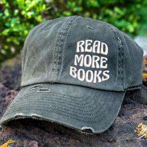 May include: A black distressed baseball cap with the text "READ MORE BOOKS" embroidered in white on the front.