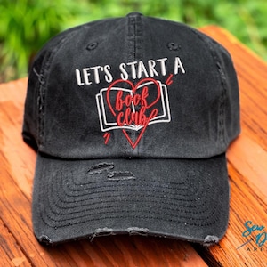 Puede incluir: Gorra de b&eacute;isbol negra desgastada con bordado blanco que dice "Let's Start a Book Club" y un coraz&oacute;n rojo con un libro dentro.