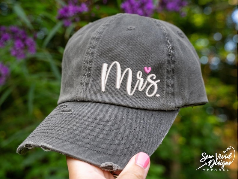 K&ouml;nnte beinhalten: Eine graue, abgenutzte Baseballkappe mit dem Wort "Mrs." in wei&szlig; gestickt, &uuml;ber dem "s" befindet sich ein kleines pinkfarbenes Herz.