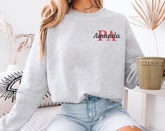 May include: A gray sweatshirt with a red and black embroidered "PA" monogram and the word "Amanda" written in black script.