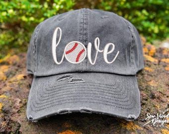 May include: A grey baseball cap with a distressed look. The cap has white embroidery that says "love" with a red and white baseball stitched in the middle of the word.