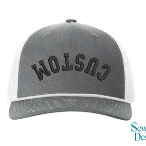 May include: Gray trucker hat with white mesh backing and a curved brim. The word "CUSTOM" is embroidered in dark gray across the front. The hat has a snap closure and a white trim. The SewVivid Designs logo is in the bottom right corner.