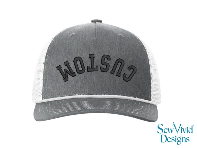 May include: Gray trucker hat with white mesh backing and a curved brim. The word "CUSTOM" is embroidered in dark gray across the front. The hat has a snap closure and a white trim. The SewVivid Designs logo is in the bottom right corner.